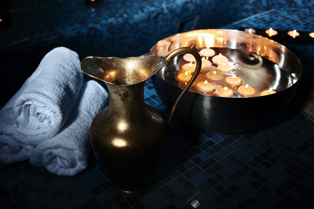 Scenery baths hammam, spa procedures. Copper jug, bowl with burning candles, white towels